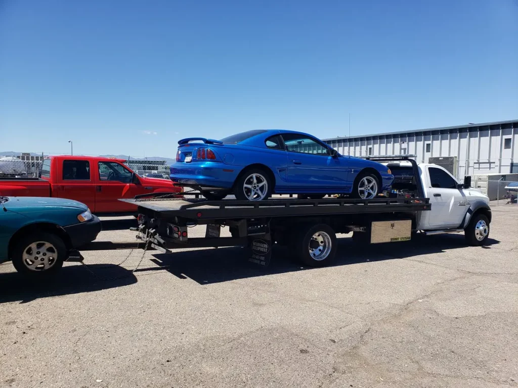 Flatbed carrying a blue Ford Mustang, junk car removal serving Boulder, CO