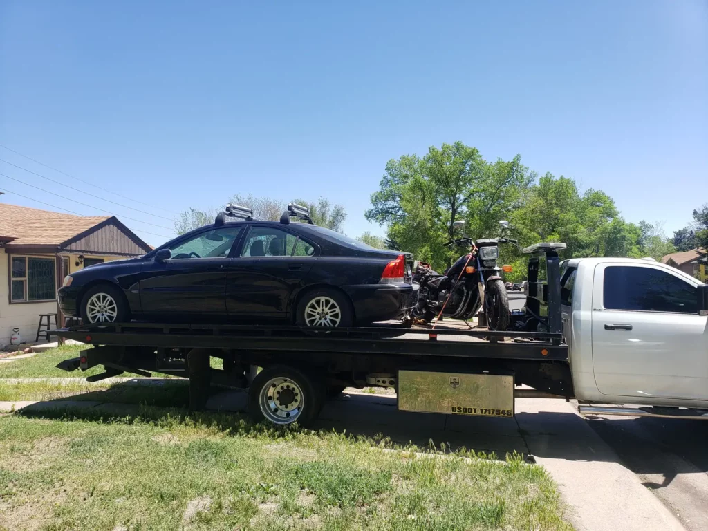 Black sedan and a motorcycle loaded on a flatbed in a neighborhood, cash for junk cars in the Castle Rock, CO area