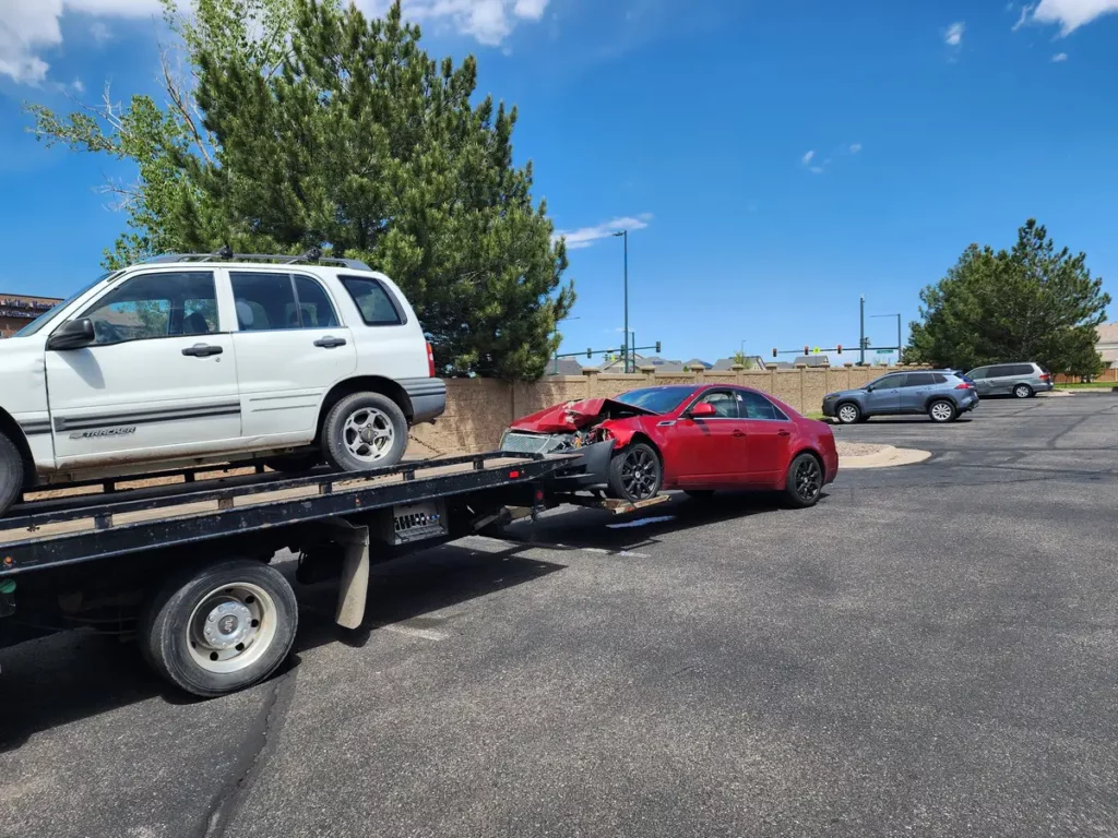 Flatbed carrying a white SUV with a wrecked red car in tow, cash for junk cars in the Englewood, CO area