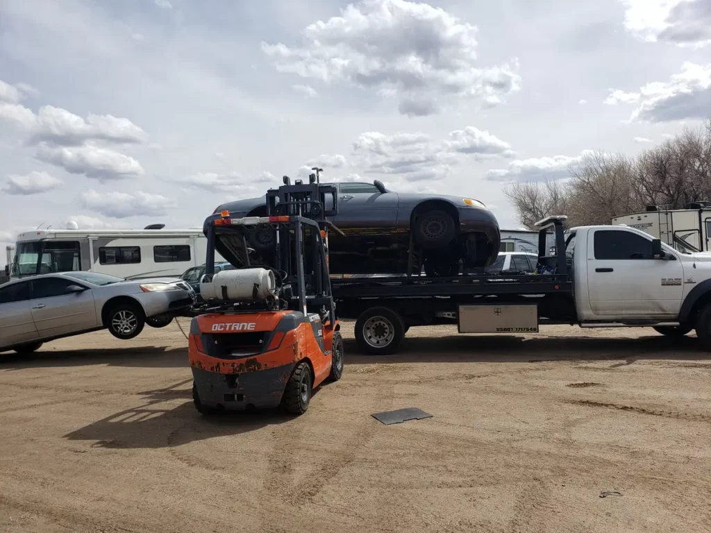 Forklift unloading a dark car from Jorge's flatbed, junk car removal serving Erie, CO