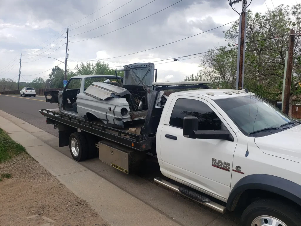Ram flatbed hauling a dismantled vehicle body for scrap, junk car removal serving Brighton, CO