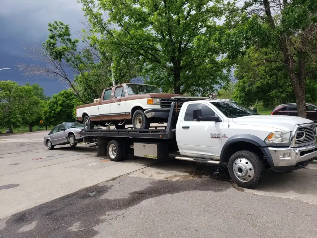 Jorge's Cash For Cars flatbed tow truck hauling a junk pickup truck and an old sedan for cash in Denver