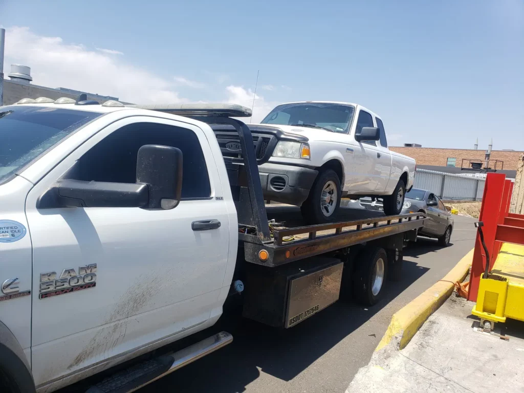 Ram flatbed tow truck hauling a white Ford pickup, junk car buyer serving Brighton, CO