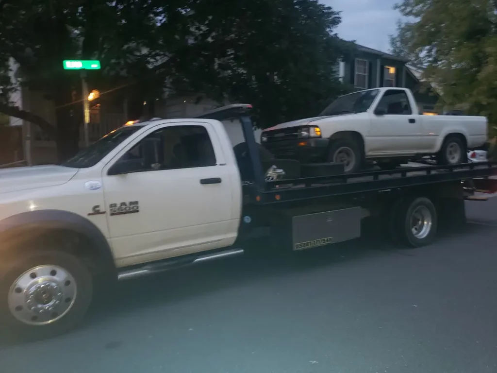 Ram flatbed hauling a white compact pickup, junk vehicle pickup serving Estes Park, CO
