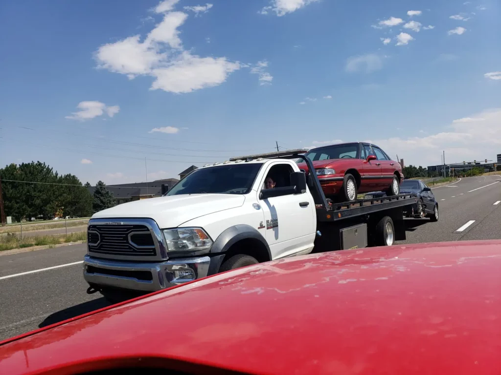 Ram flatbed hauling a red car down the road, junk vehicle pickup serving Castle Rock, CO