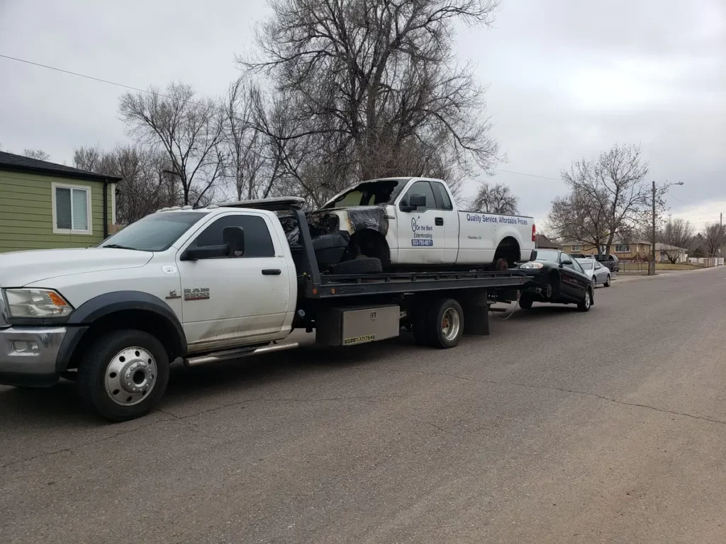 Ram flatbed hauling a white pickup with a car in tow, junk car buyer serving Boulder, CO