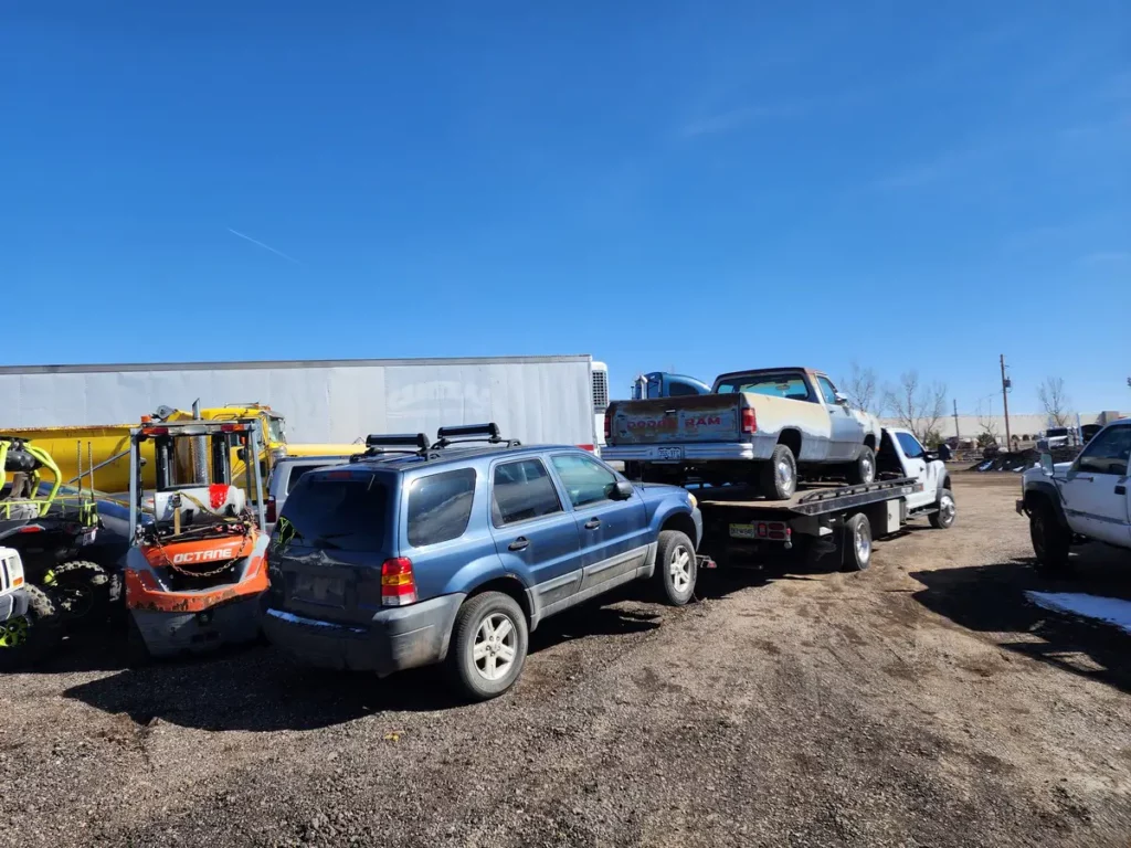 Blue SUV and other junk vehicles waiting for pickup beside Jorge's flatbed, junk car removal serving Westminster, CO