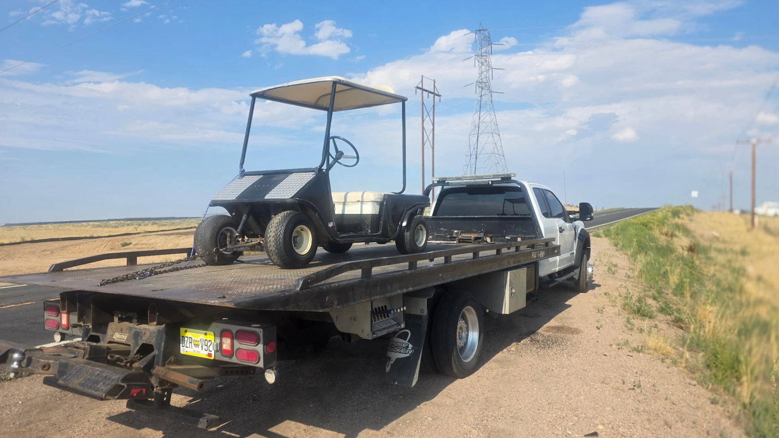 Jorge's Cash For Cars flatbed tow truck hauling a golf cart near Denver, Colorado