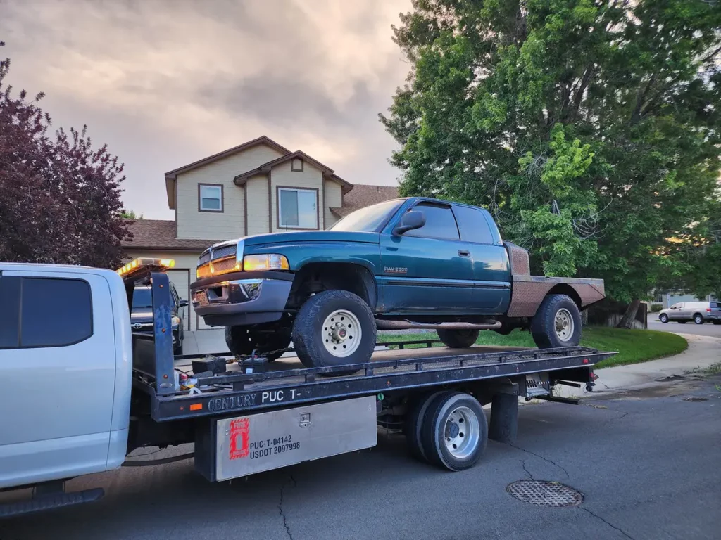 Flatbed carrying a green Dodge Ram pickup in a neighborhood, we buy junk cars in the Erie, CO area