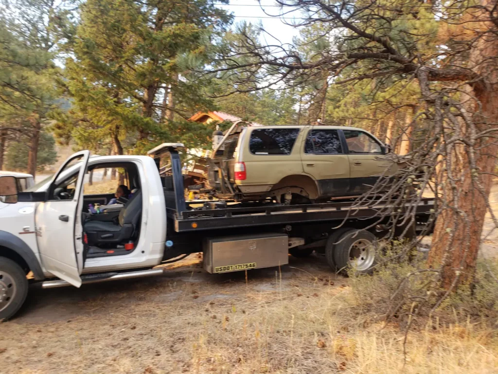 Flatbed loading a rusty old SUV among pine trees, we buy junk cars in the Highlands Ranch, CO area