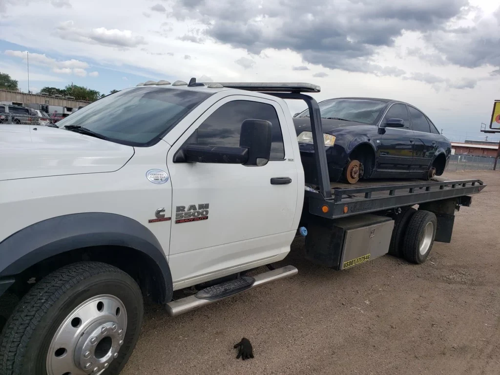 Wrecked sedan with a missing wheel loaded on Jorge's flatbed tow truck, we buy wrecked cars in Denver