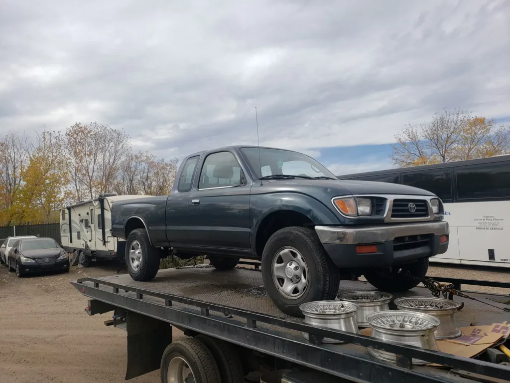 Old green pickup truck on the bed of Jorge's tow truck, junk car removal serving Henderson, CO